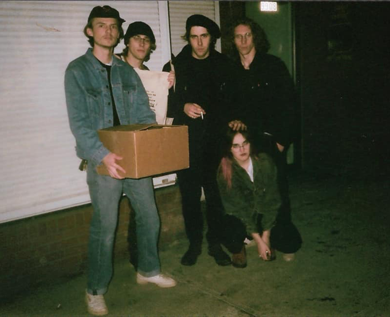 five bandmates pose at night in front of garage holding boxes
