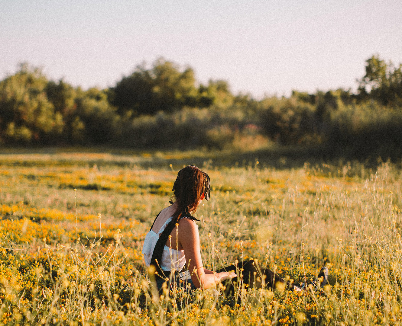 woman sits in field of yellow flowers
