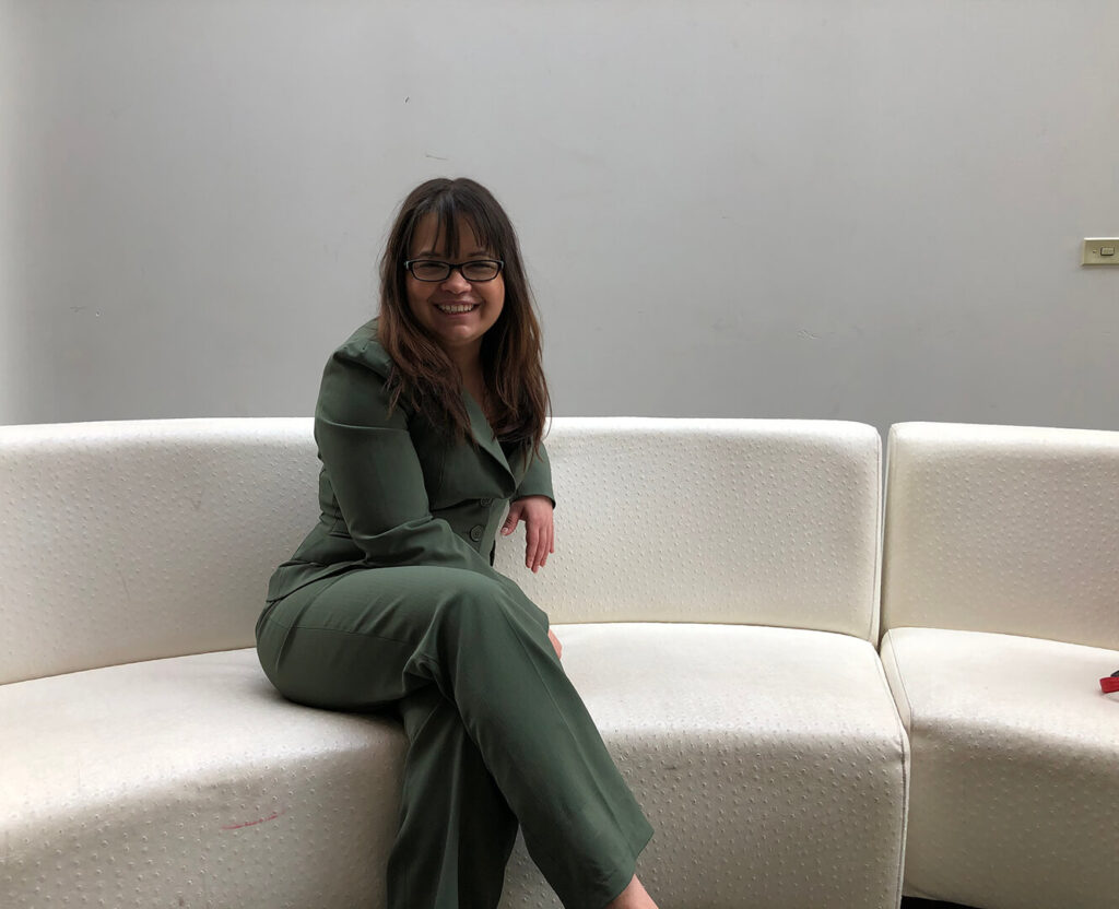 Woman sits on white couch smiling for photo