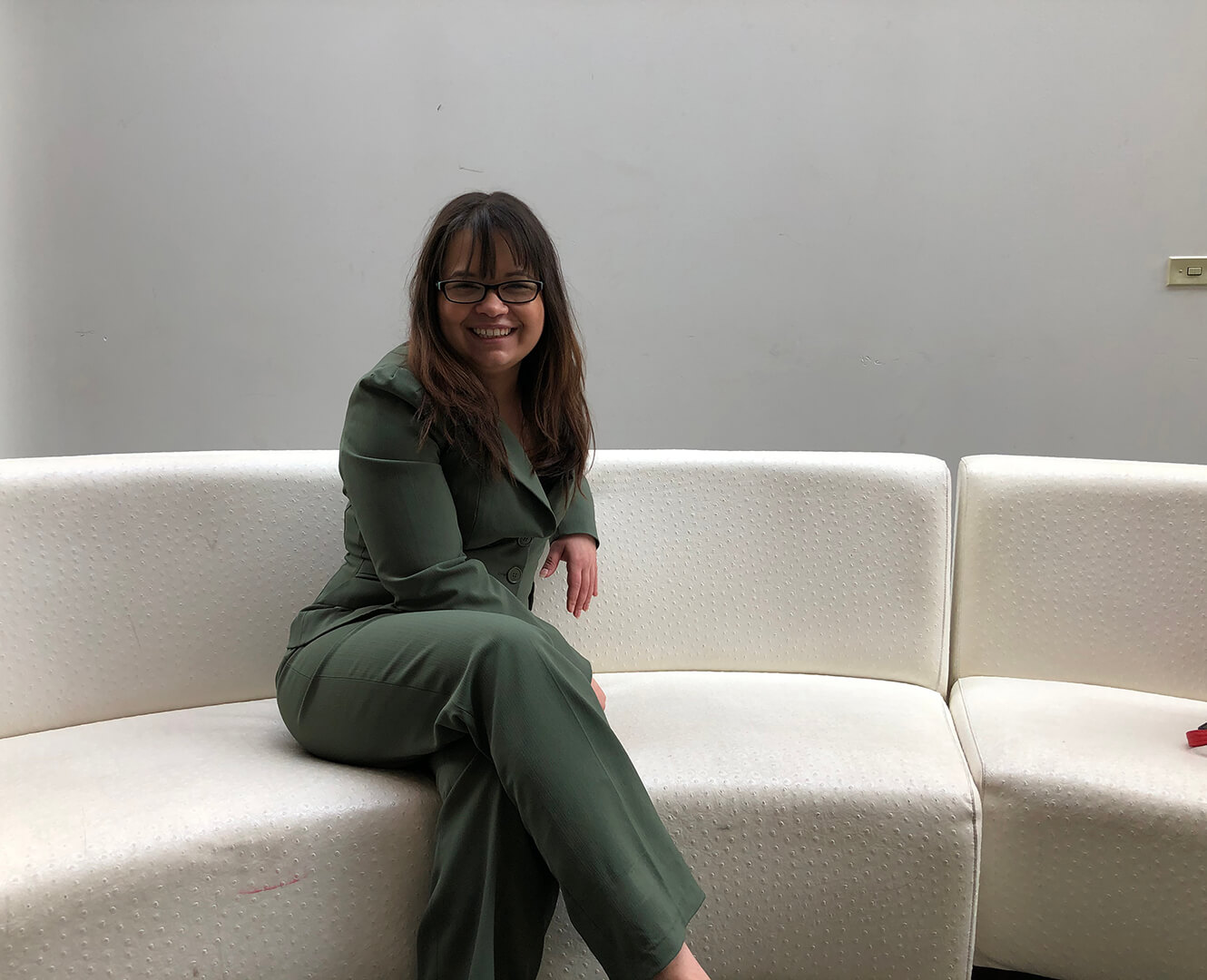 Woman sits on white couch smiling for photo