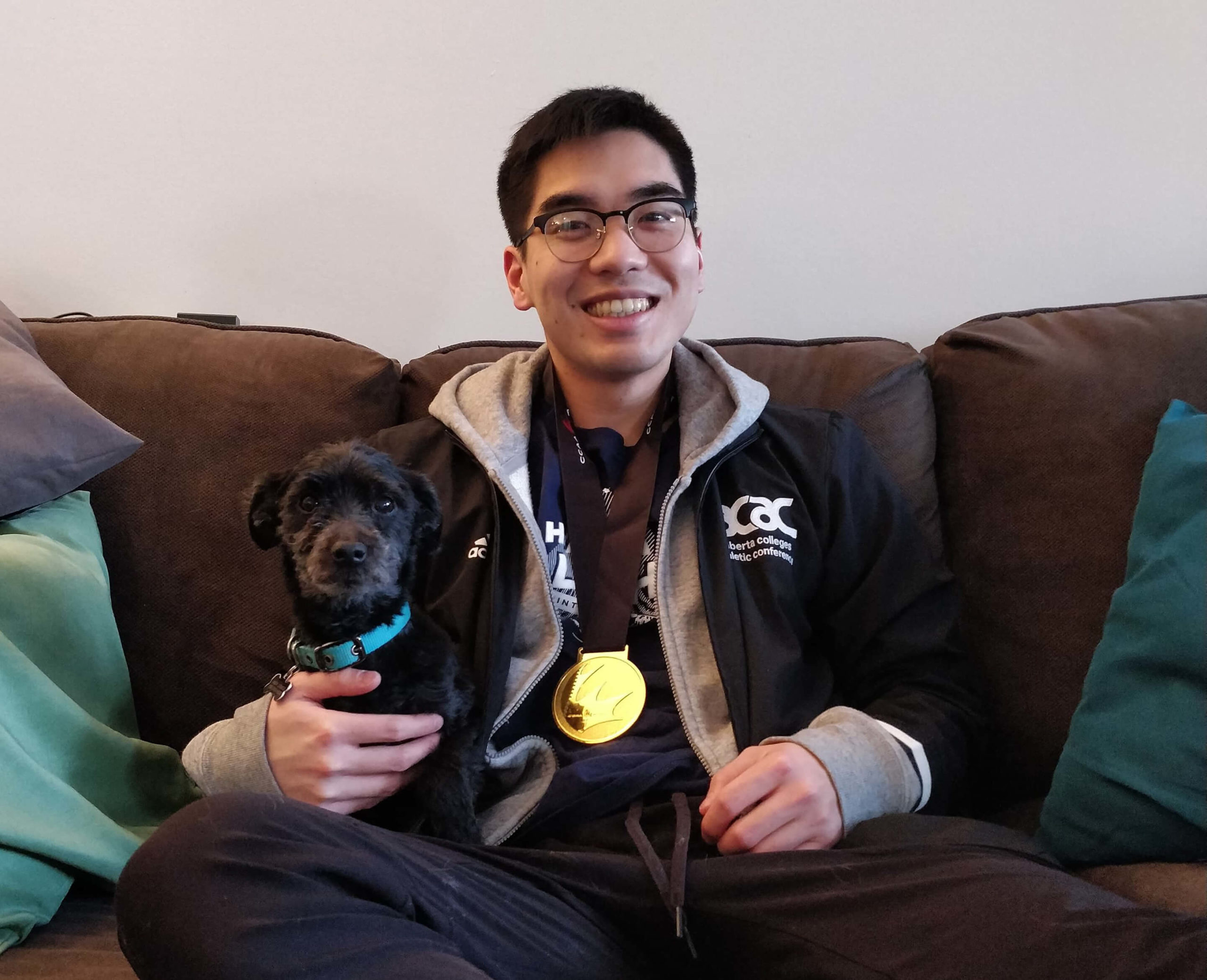 badminton champion of NAIT Alex Fung sits on couch with his dog.