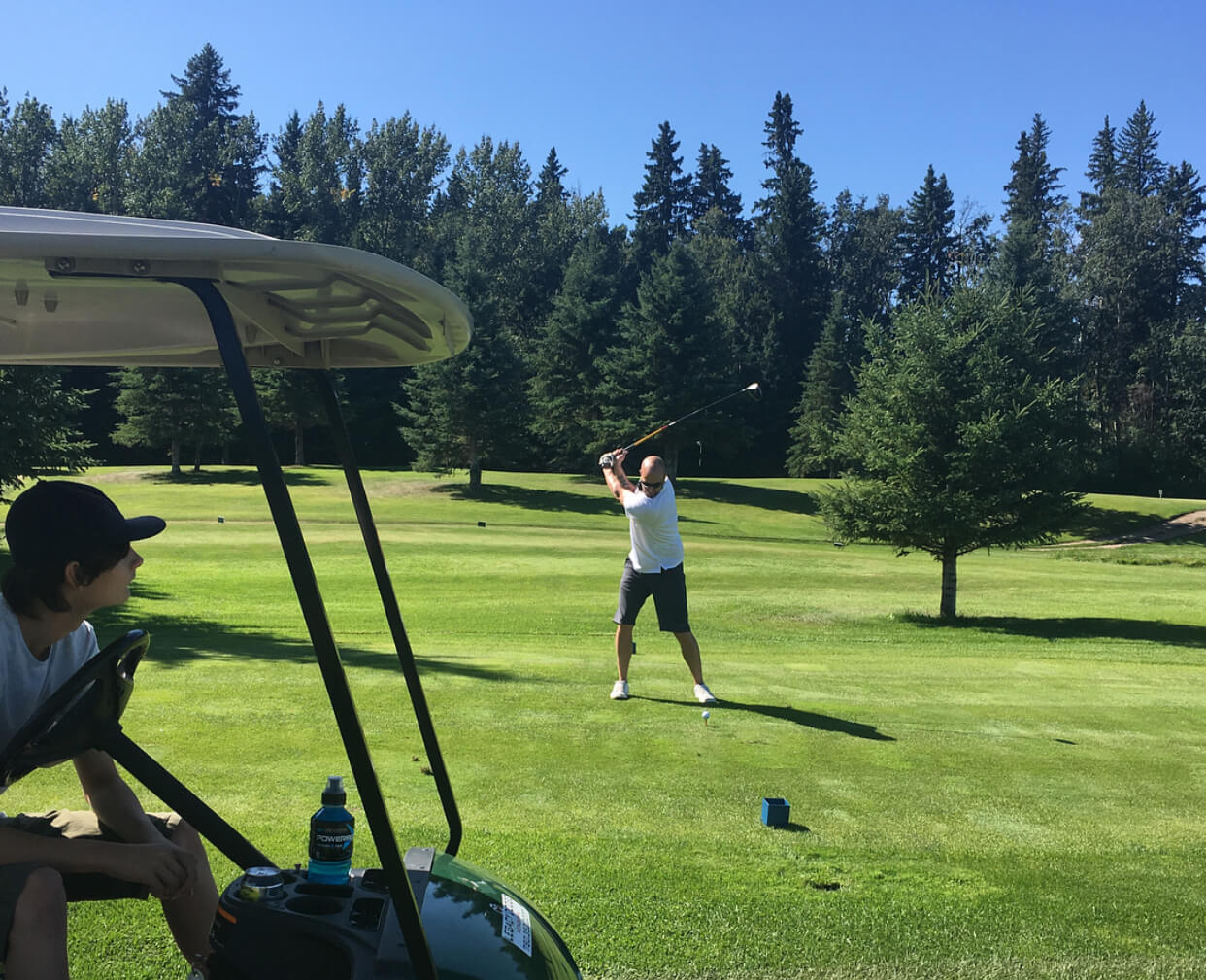Man plays golf on green course in Alberta in summer months.