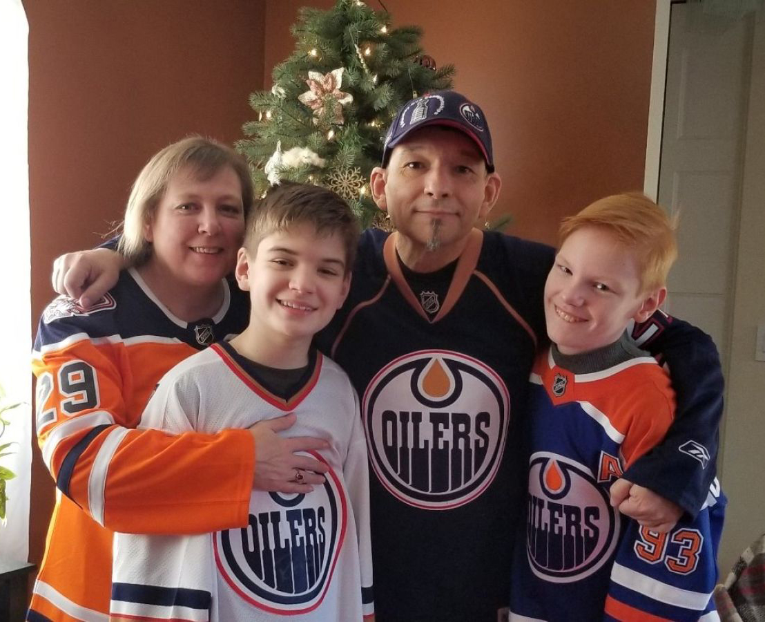mother, father and two stands stand in front of Christmas tree wearing Oiler's hockey jersey's