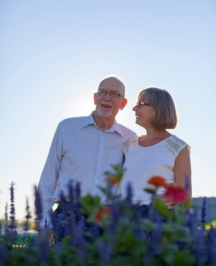 Elderly couple smile stand in field of flowers