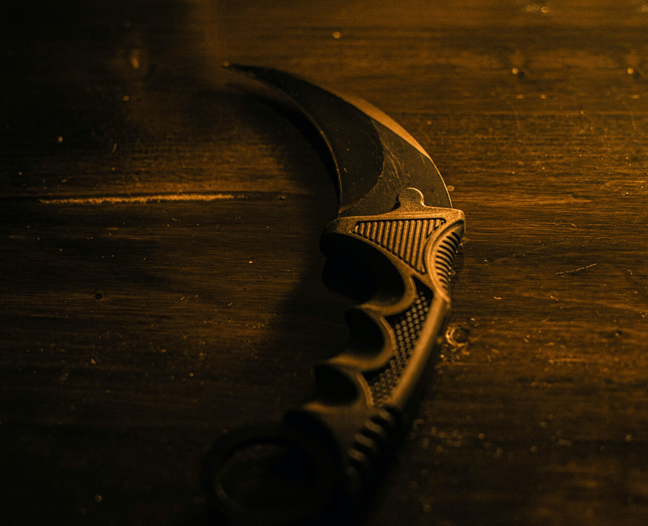 A knife sits on a wood table in a dark room