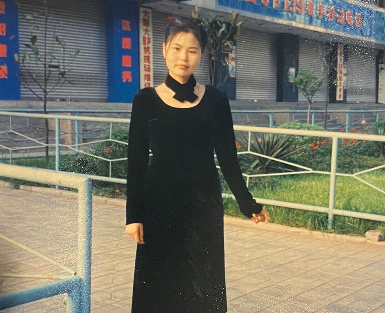 Hong stands in black dress on street in China.