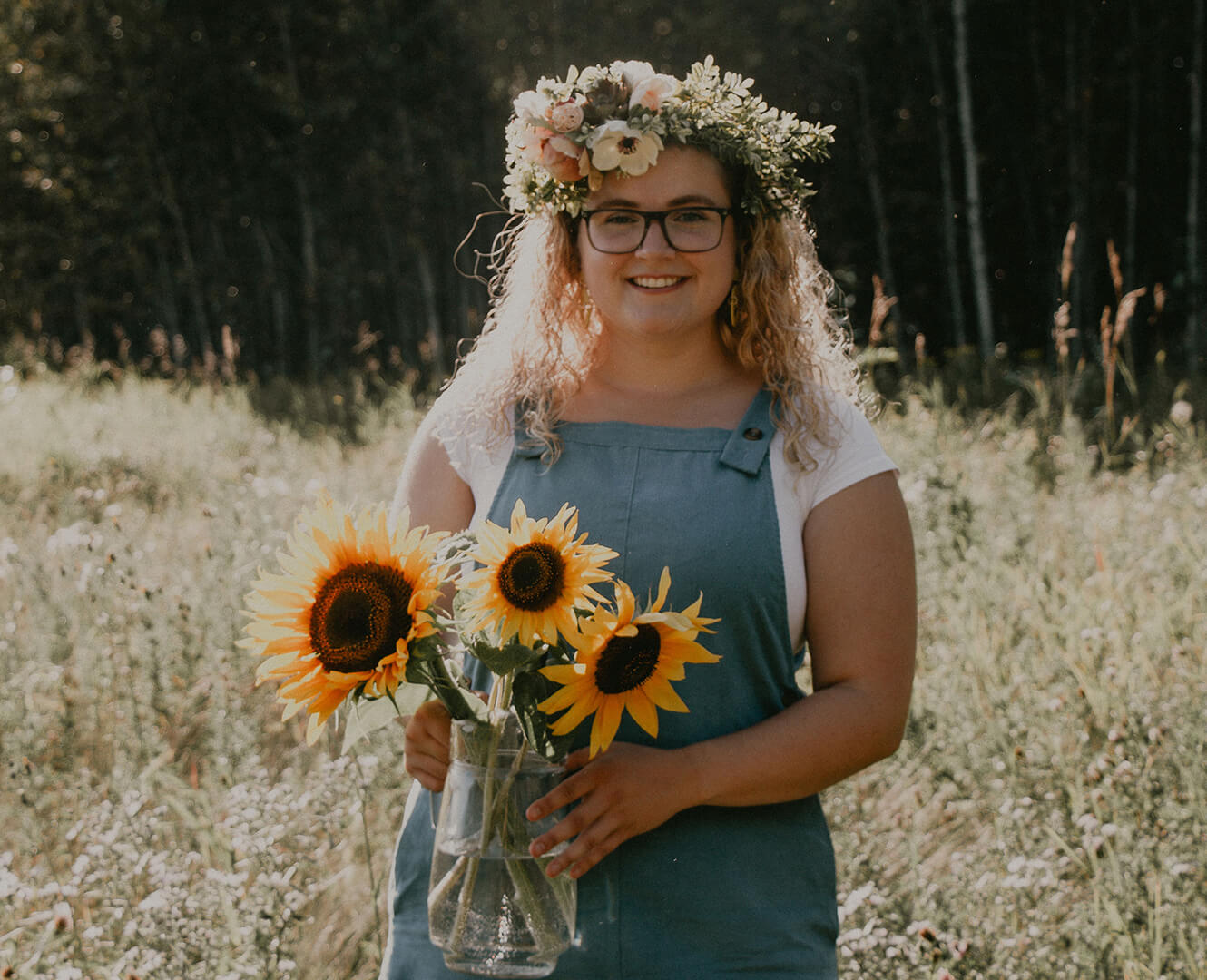 Natasha Martinez stands in wheat field holding bouquet of sunflowers