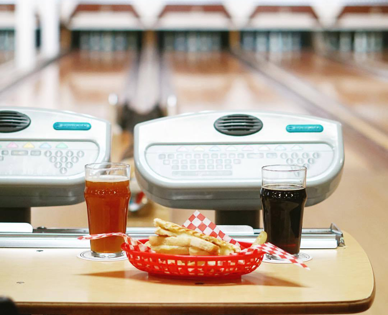 A bowling lane with a table and fries with 2 glasses of pop