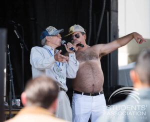 Two men one shirtless sing on stage