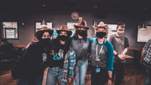 Group of CAB employees wearing cowboy hats and masks in a bar.