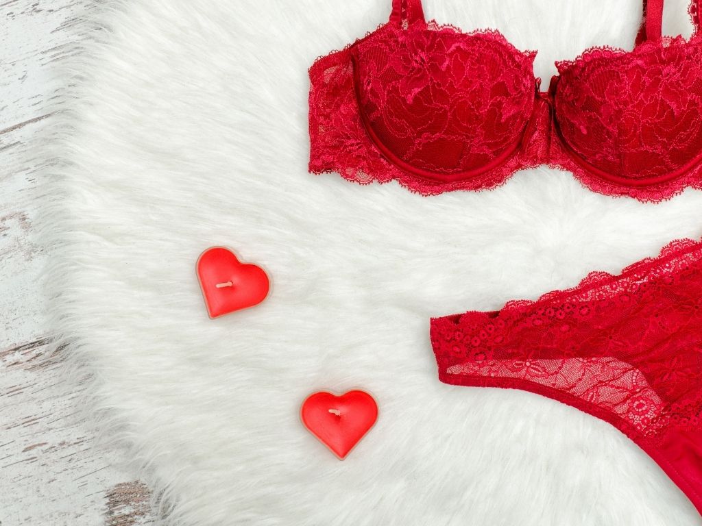 a red bra and panties on a fluffy white carpet next to two red heart shaped candles
