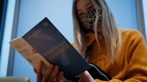 a woman wearing a leopard print masks reads a brocure about IUDs