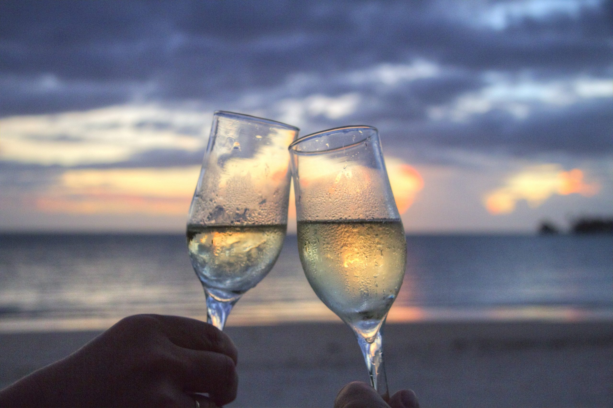 two glasses of champagne clinking on a beach