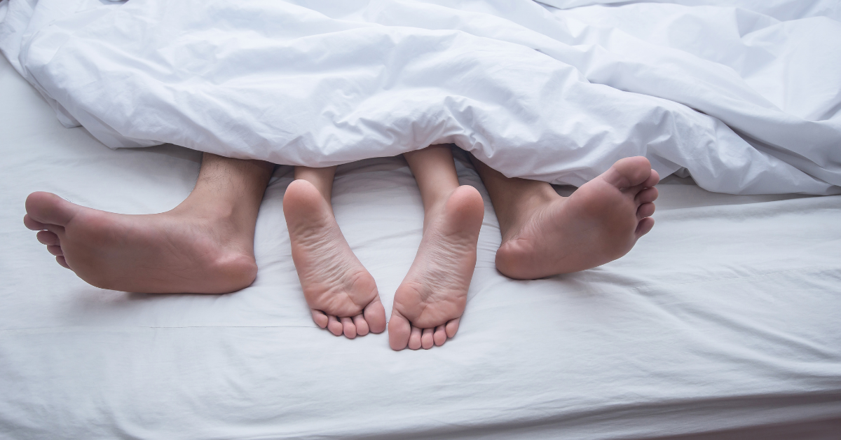 two pairs of feet sticking out the end of a white blanket