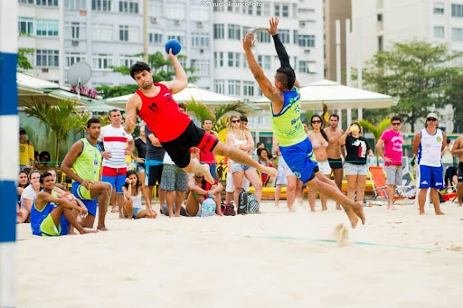 Two men playing beach handball. There is a crow of people watching them.