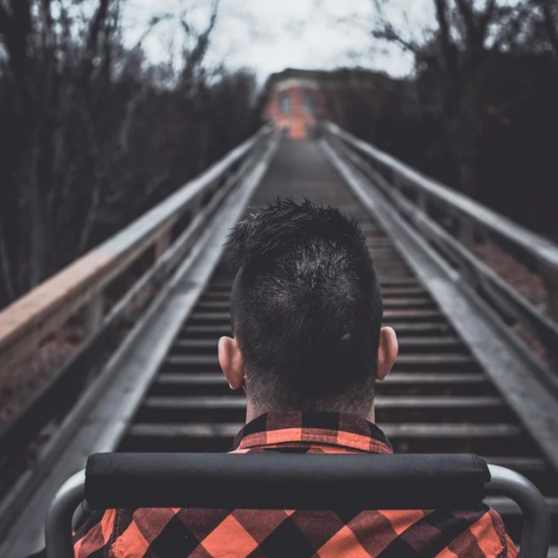 man in wheelchair wearing plaid shirt overlooks a railroad track