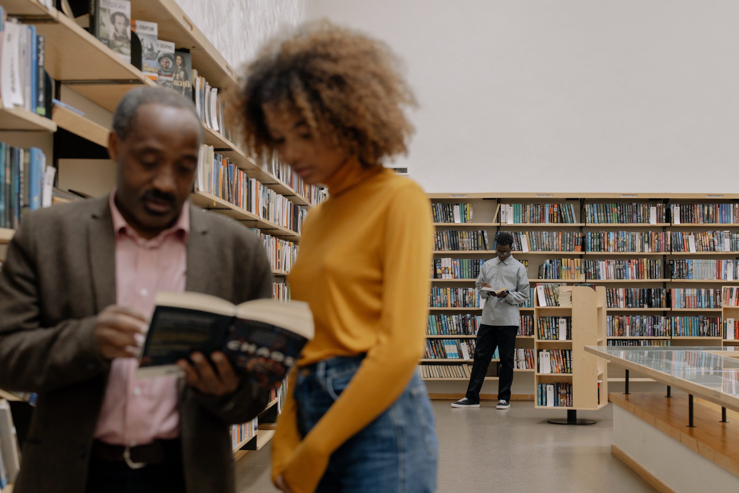 Older black man and younger black woman read a book in a library. They are slightly out of focus.