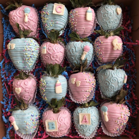 A box of chocolate covered strawberries in blue and pink icing. 