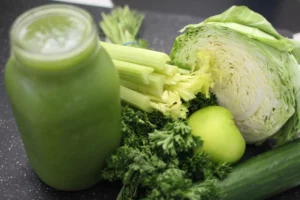A jarred green smoothie. Some celery, cabbage, and other greens sit beside it. 