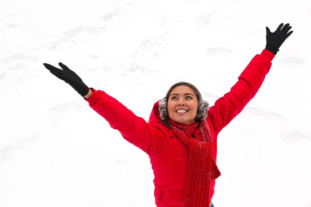 A woman in a red coat and earmuffs throwing her hand in the air.