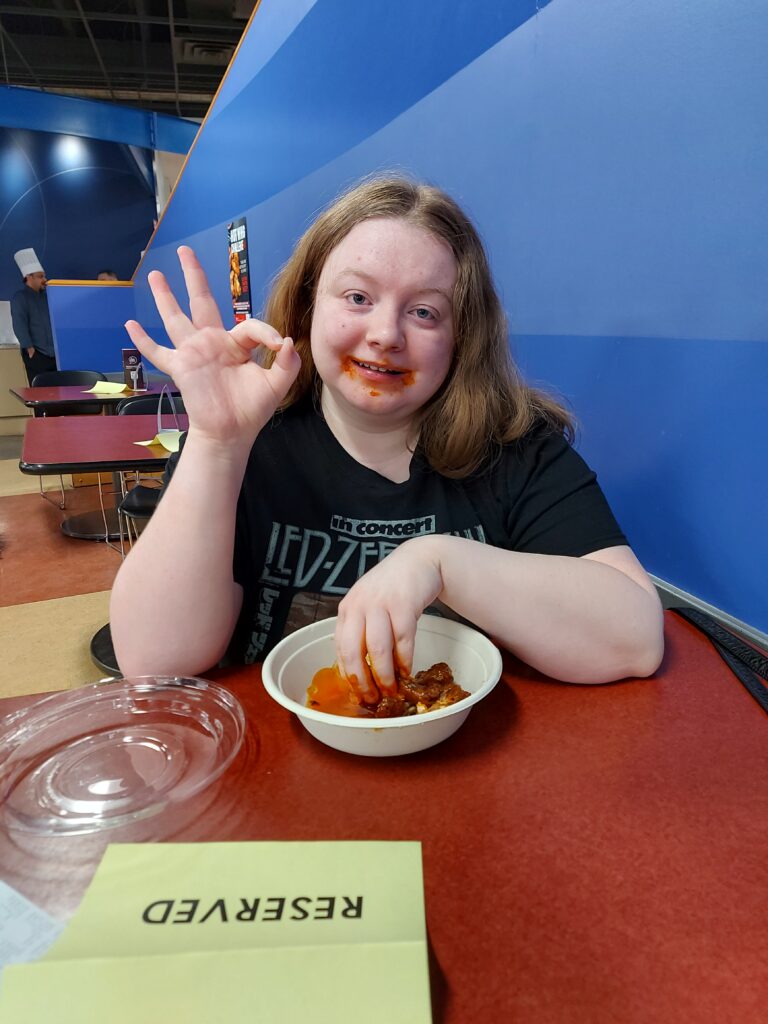 A redheaded girl poses with hot wing sauce all over her face. She is making an a-okay sign. 