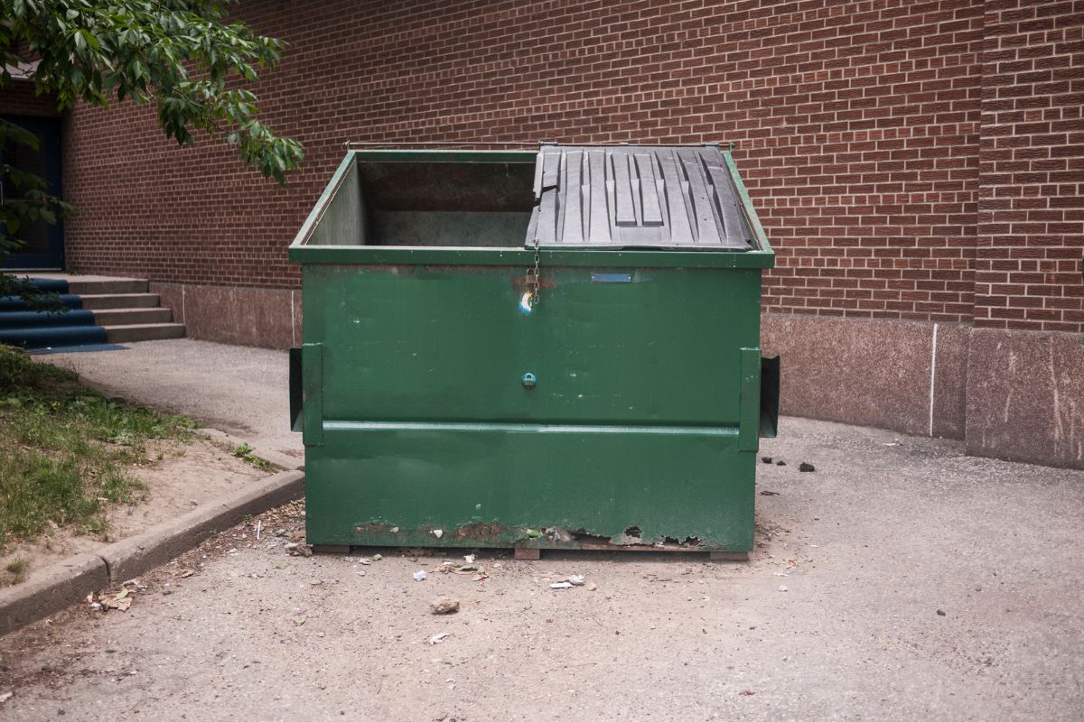 A dumpster sits open in front of a brick wall.