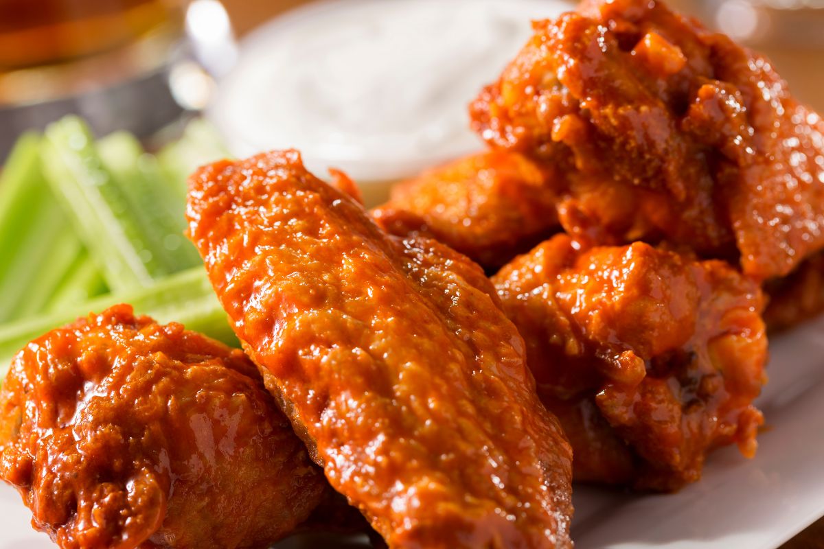 Four spicy chicken wings sit on a plate with ranch and celery in the background.