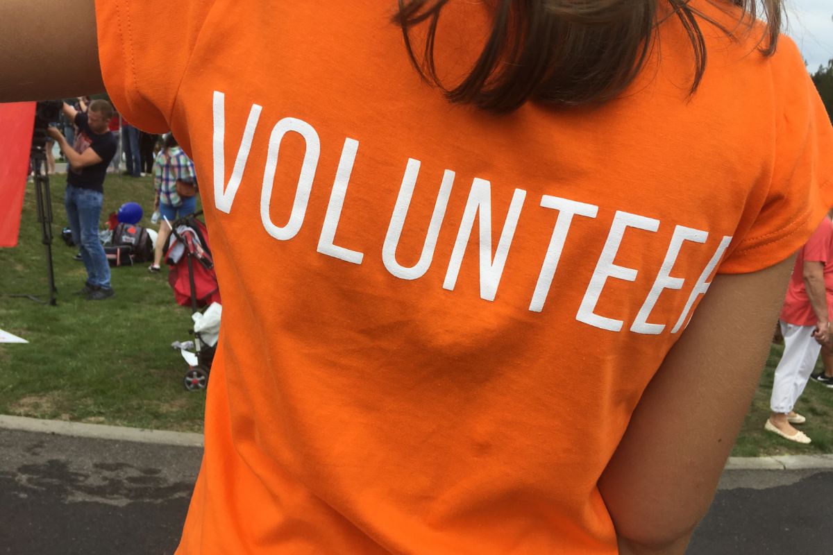 Person wearing an orange shirt with "Volunteer" printed on their back poses