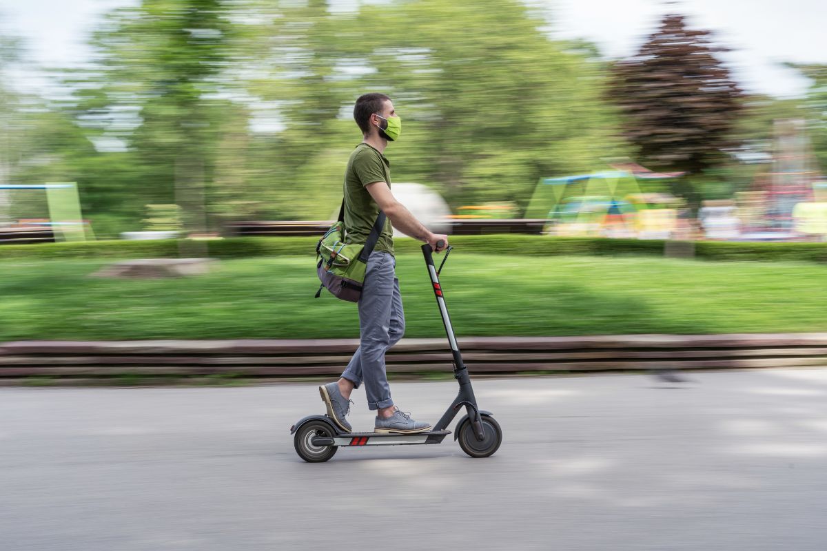 A man wearing a green shirt and face mask is riding an e-scooter in spring.