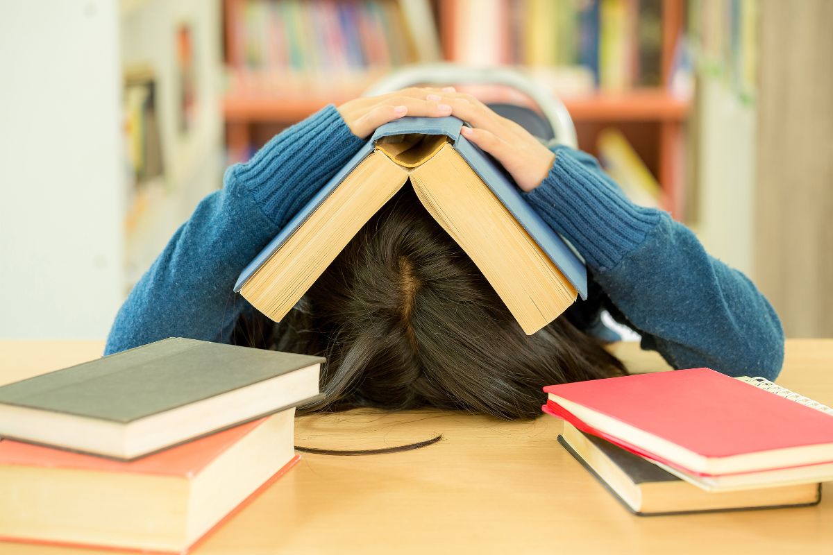 a student has their head down on a desk with a book spread on top of it.