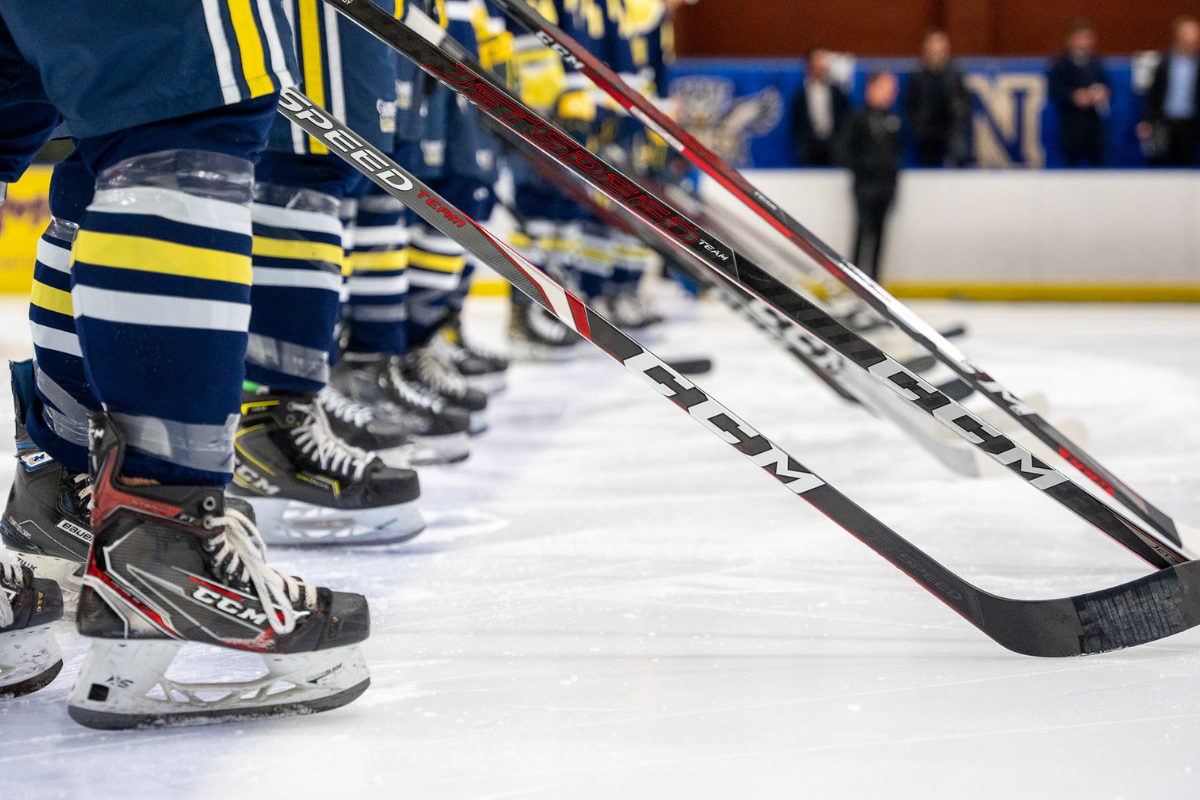 Hockey players stand in a row, pictured from the knee down. Their sticks are out in front of them.