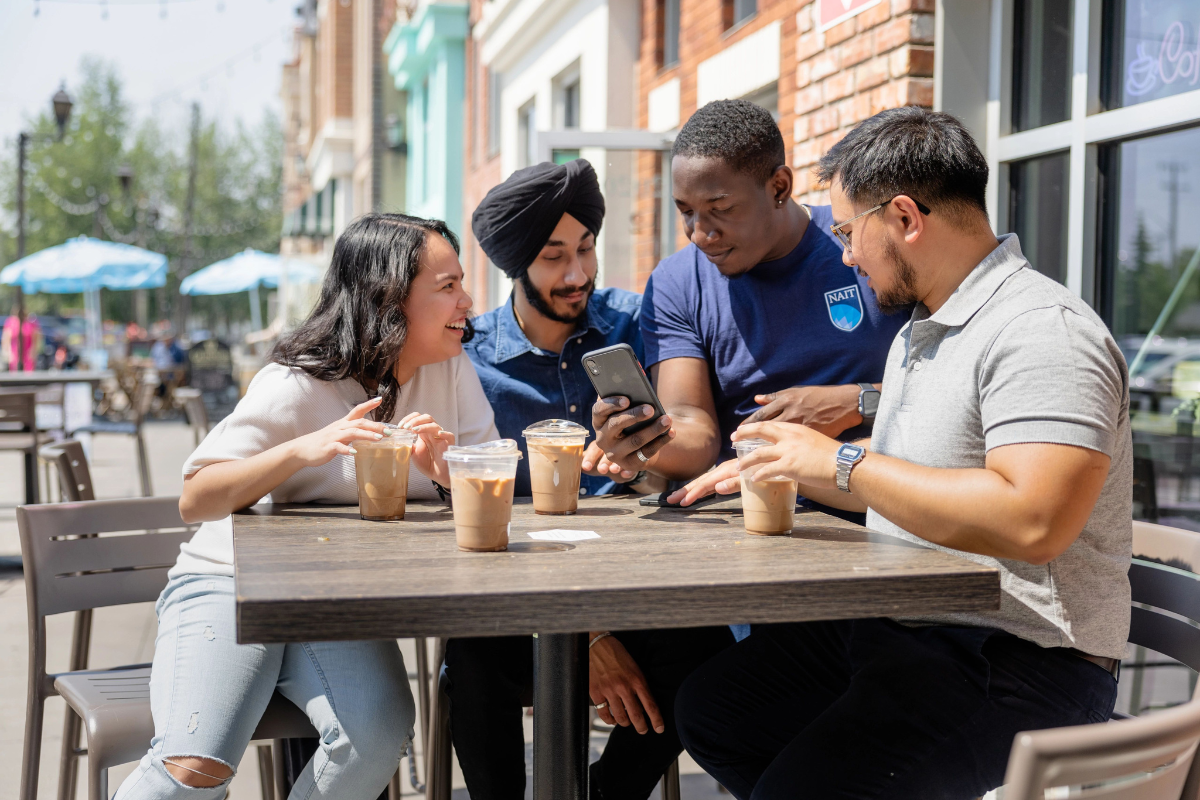 A group of students sitting with iced coffees at a table. They are laughing and looking happy.