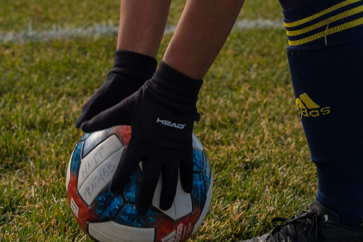 a pair of hands in soccer gloves reach down to grab a soccer ball