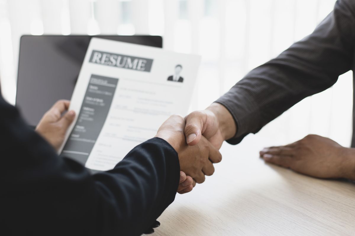 Two people shaking hands. One person holds a resume.