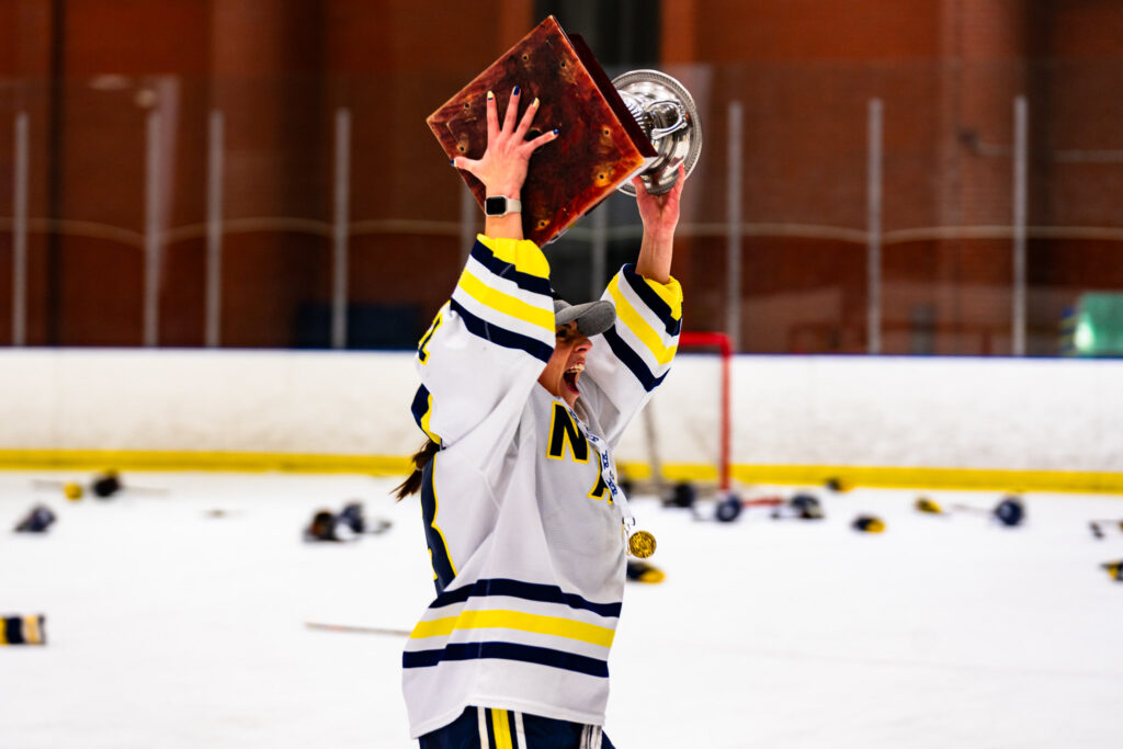 a female hockey player holds a trophy and has her arms up in the air