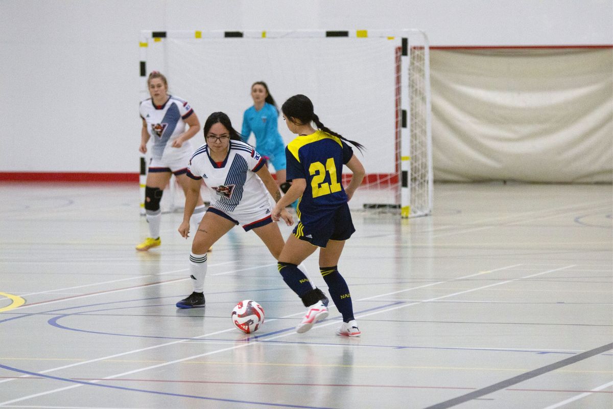 Women from two opposing teams play futsal, a type of soccer played indoors.