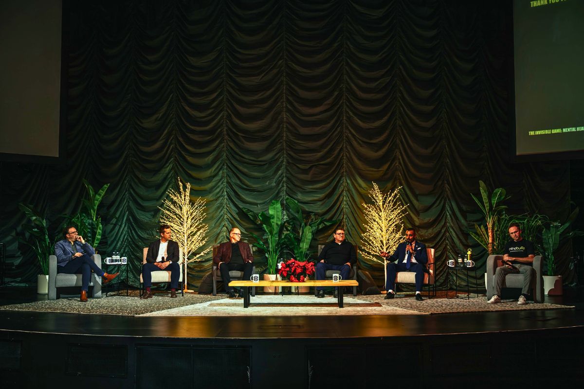 A group of men sit in chairs on a dimly lit stage.