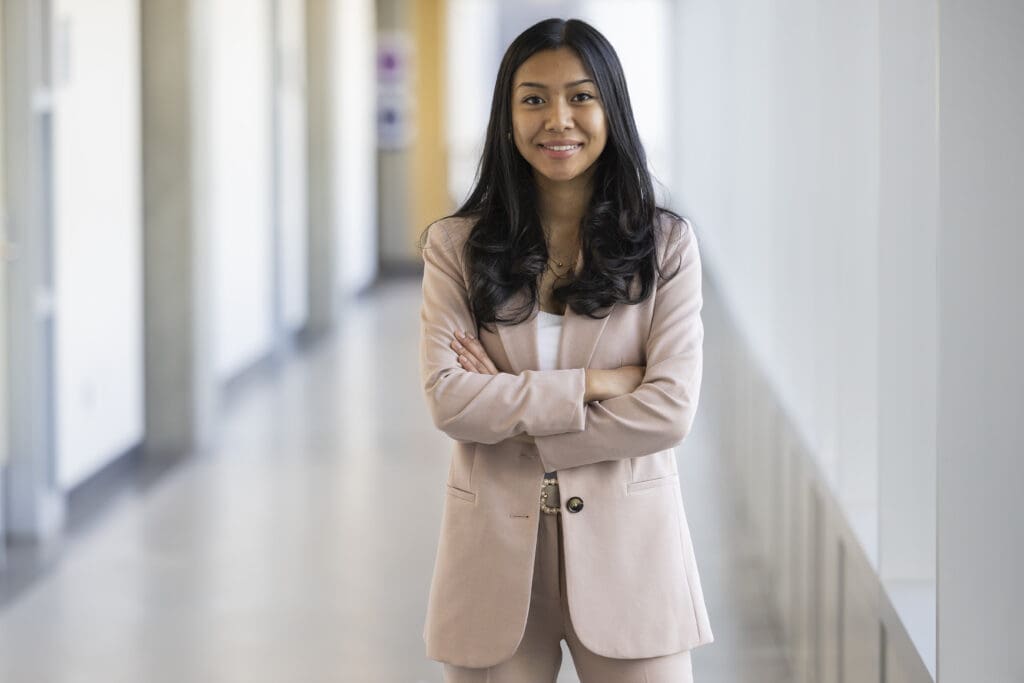 A tan woman in a beige suit poses with her arms crossed. 
