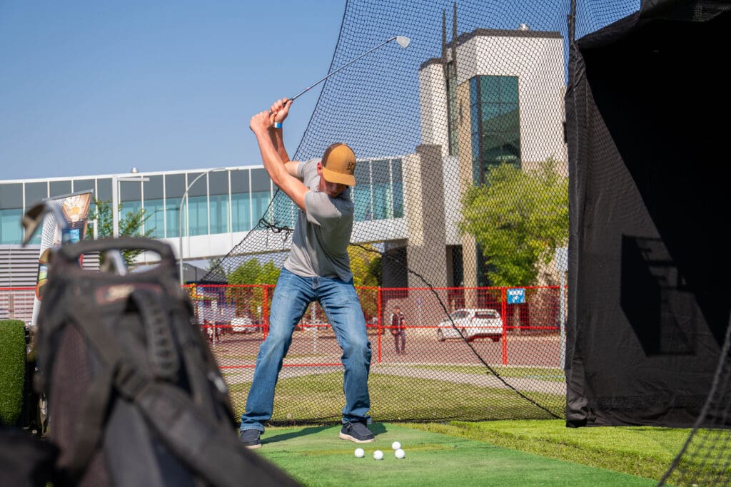 A man swings a golf club, aiming at a target. 